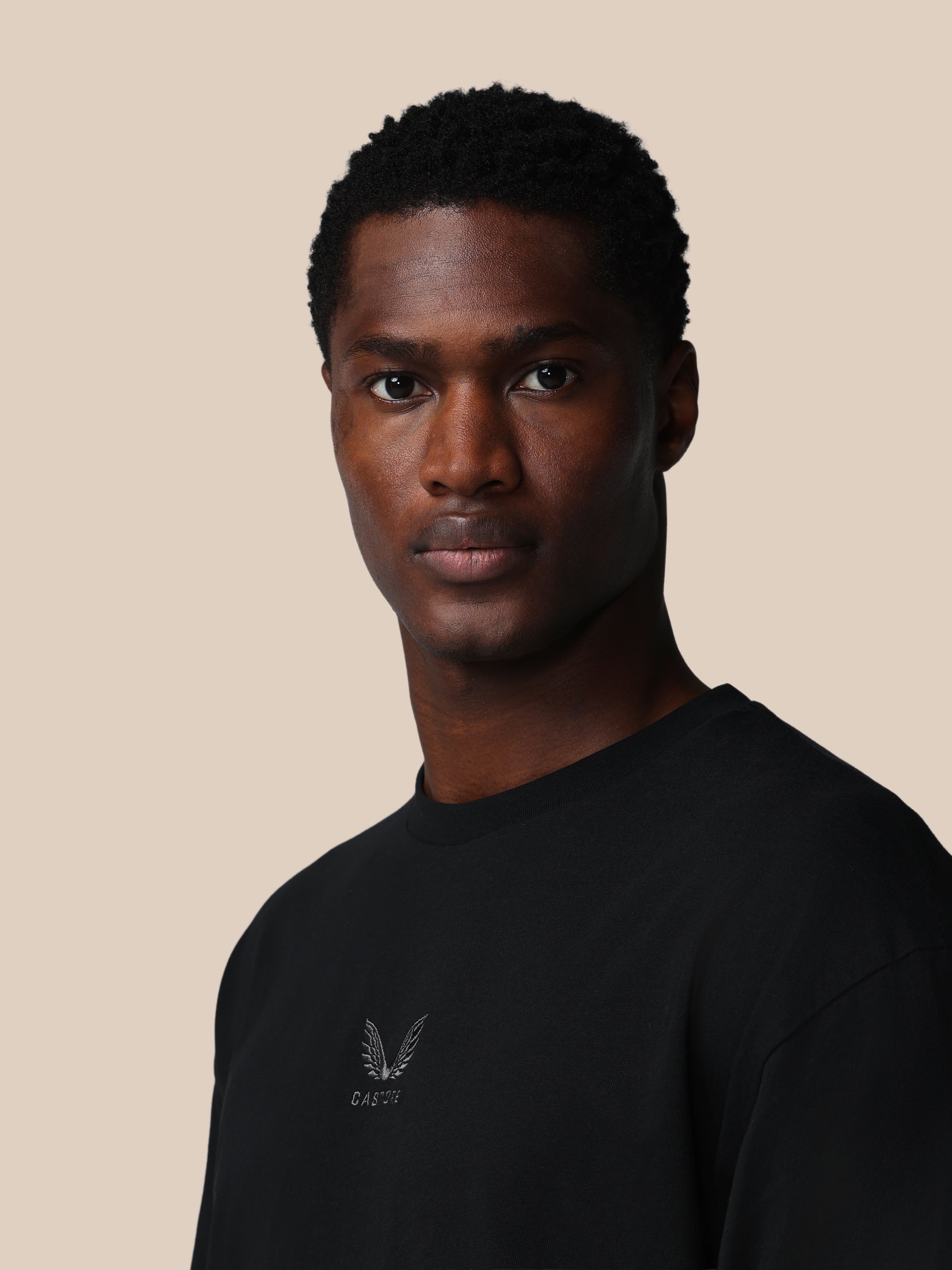 Man wearing a black t-shirt with a logo on a beige background