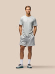 A man modeling a light gray short-sleeve t-shirt and matching light gray shorts against a solid beige background.