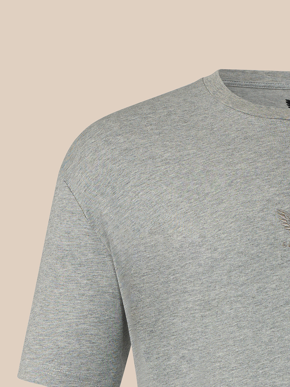 Close-up of a light heather gray crewneck t-shirt showing the shoulder, sleeve, and chest area against a solid beige background.