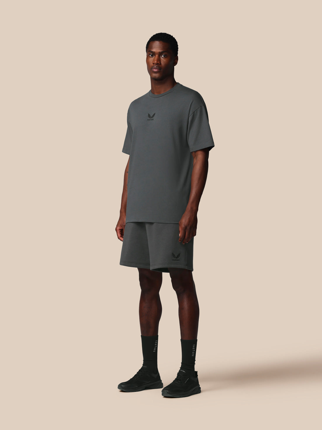 Man wearing a gray t-shirt and shorts set with a logo on a beige background