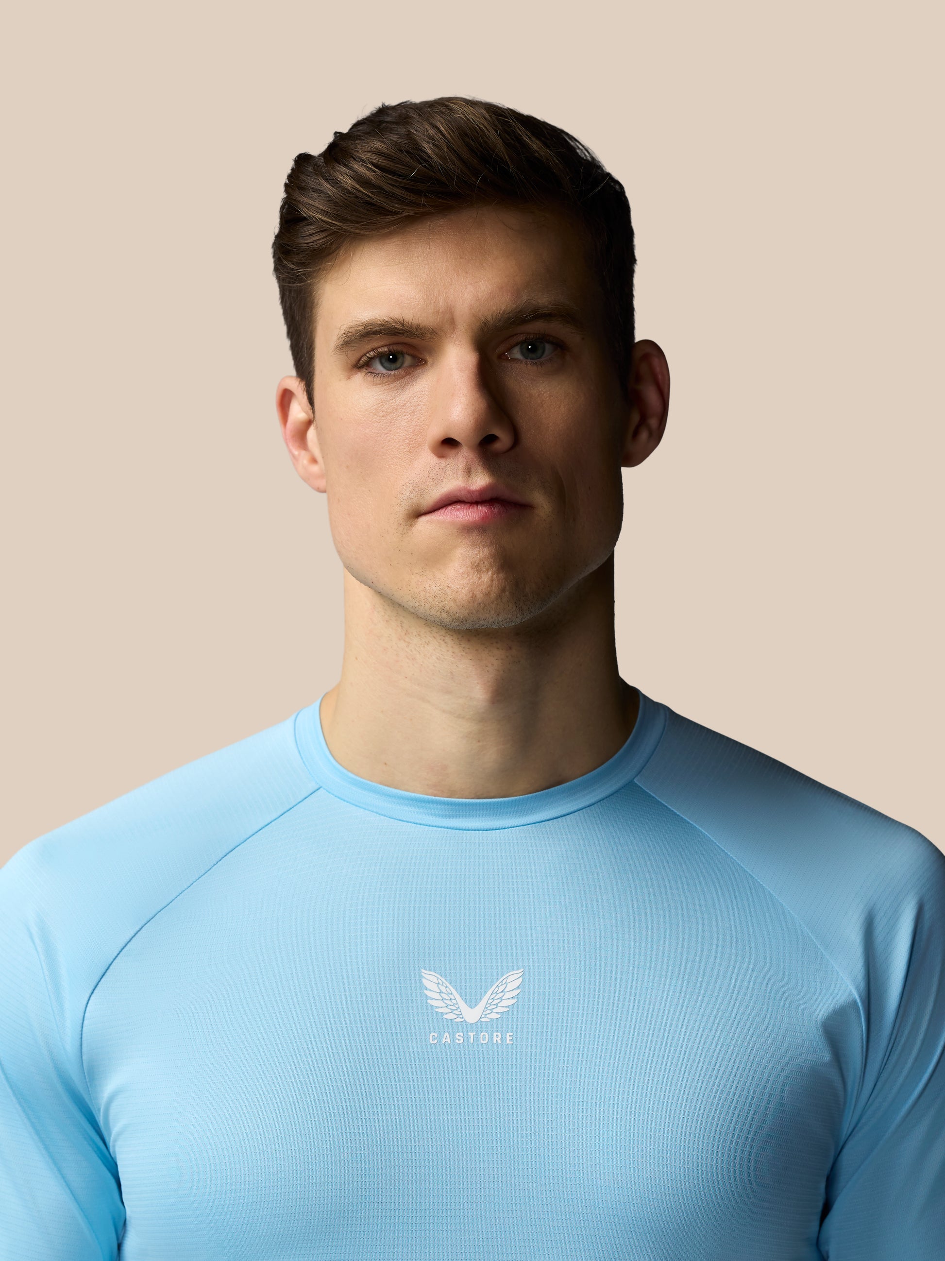 Man wearing a light blue athletic shirt with a logo on a beige background