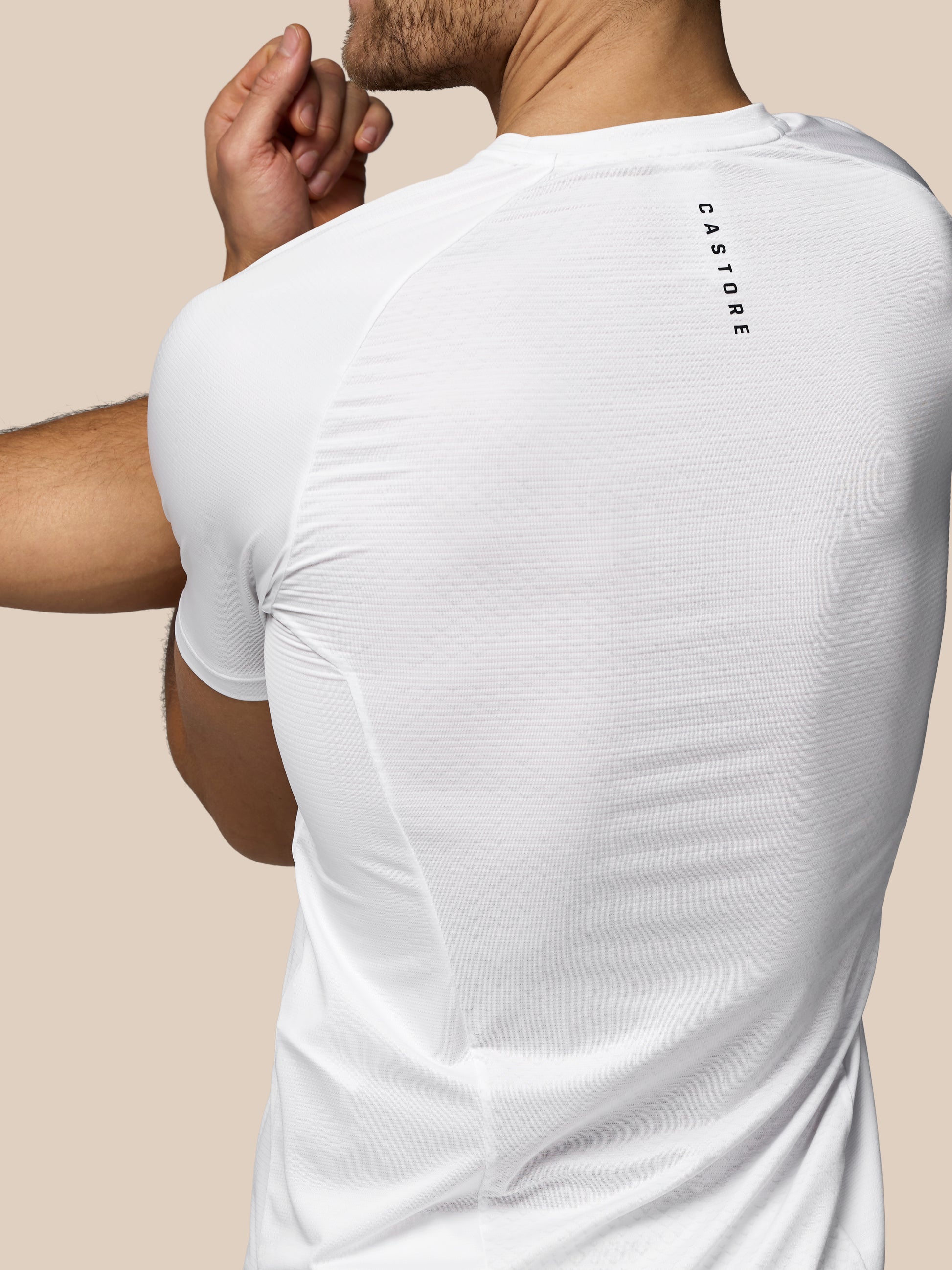 Person wearing a white t-shirt with 'CASTORE' branding on the back against a beige background