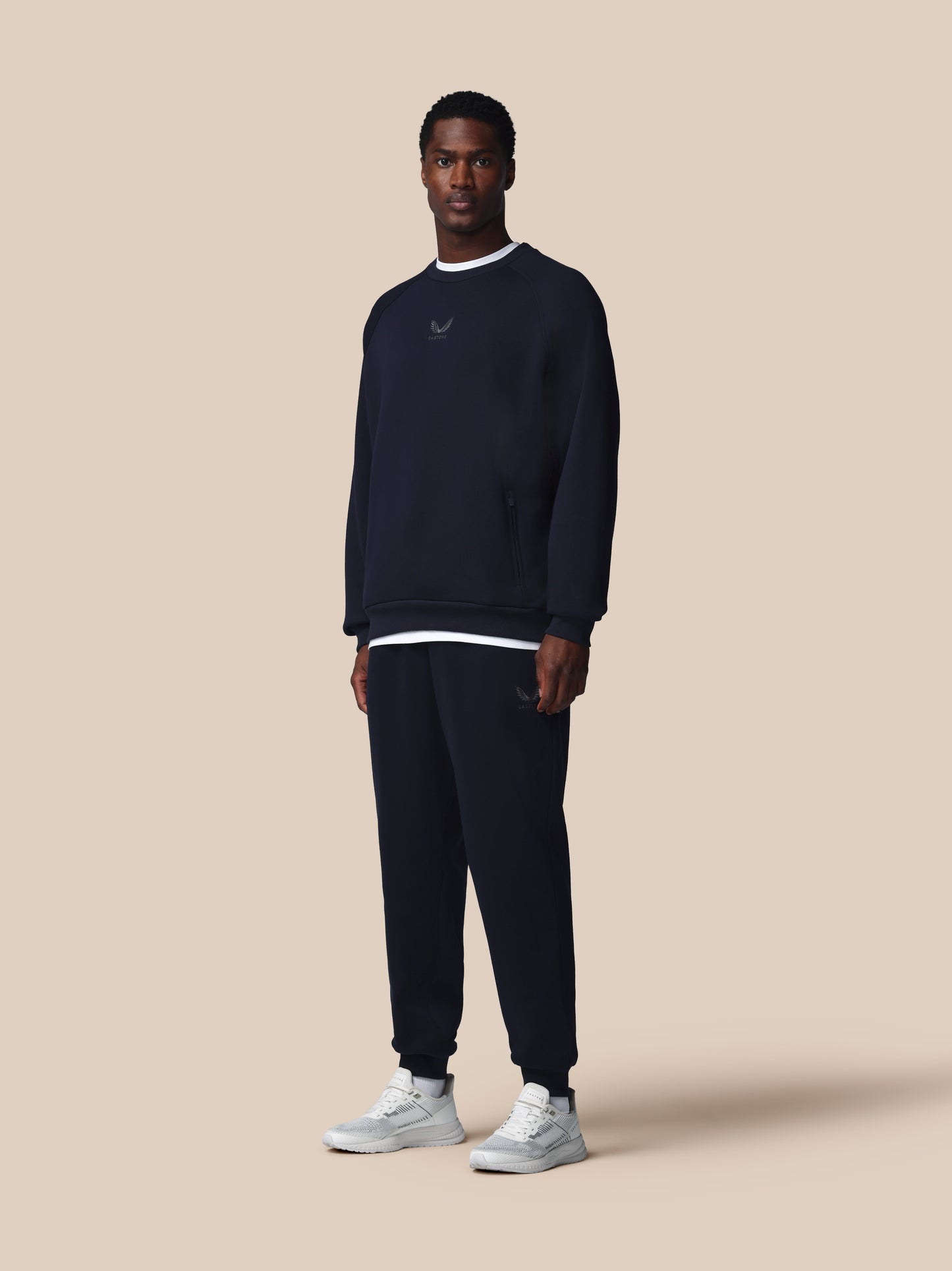 Man wearing a navy blue sweatshirt and pants with a logo on a beige background