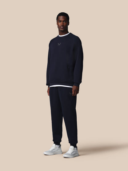 Man wearing a navy blue sweatshirt and pants with a logo on a beige background