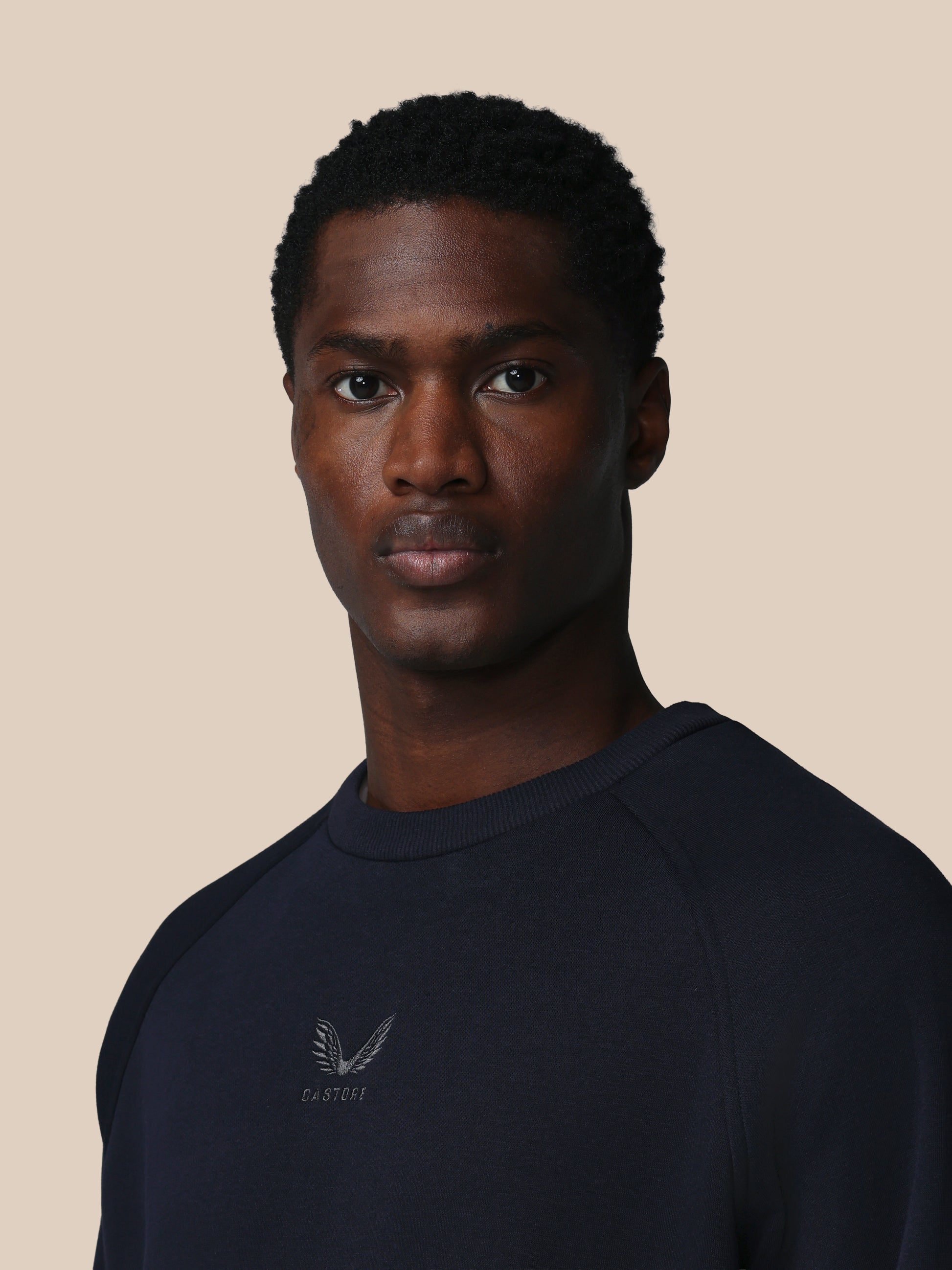 Man wearing a black sweatshirt with a logo on a beige background