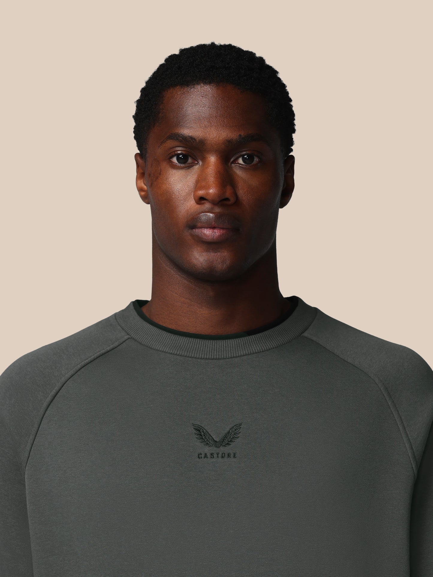 Man wearing a dark gray sweatshirt with a logo on a beige background