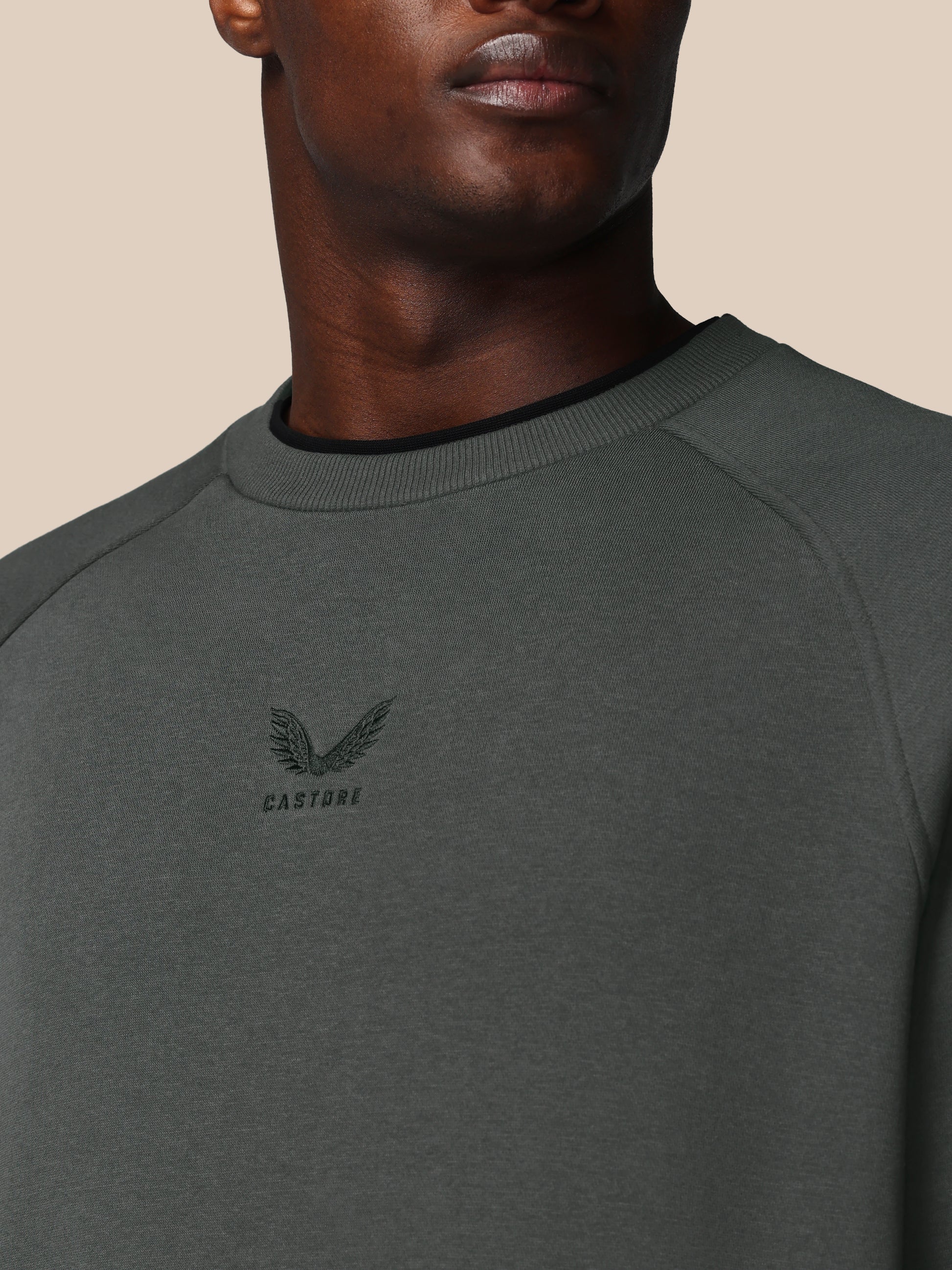 Person wearing a dark gray sweatshirt with a logo on a beige background
