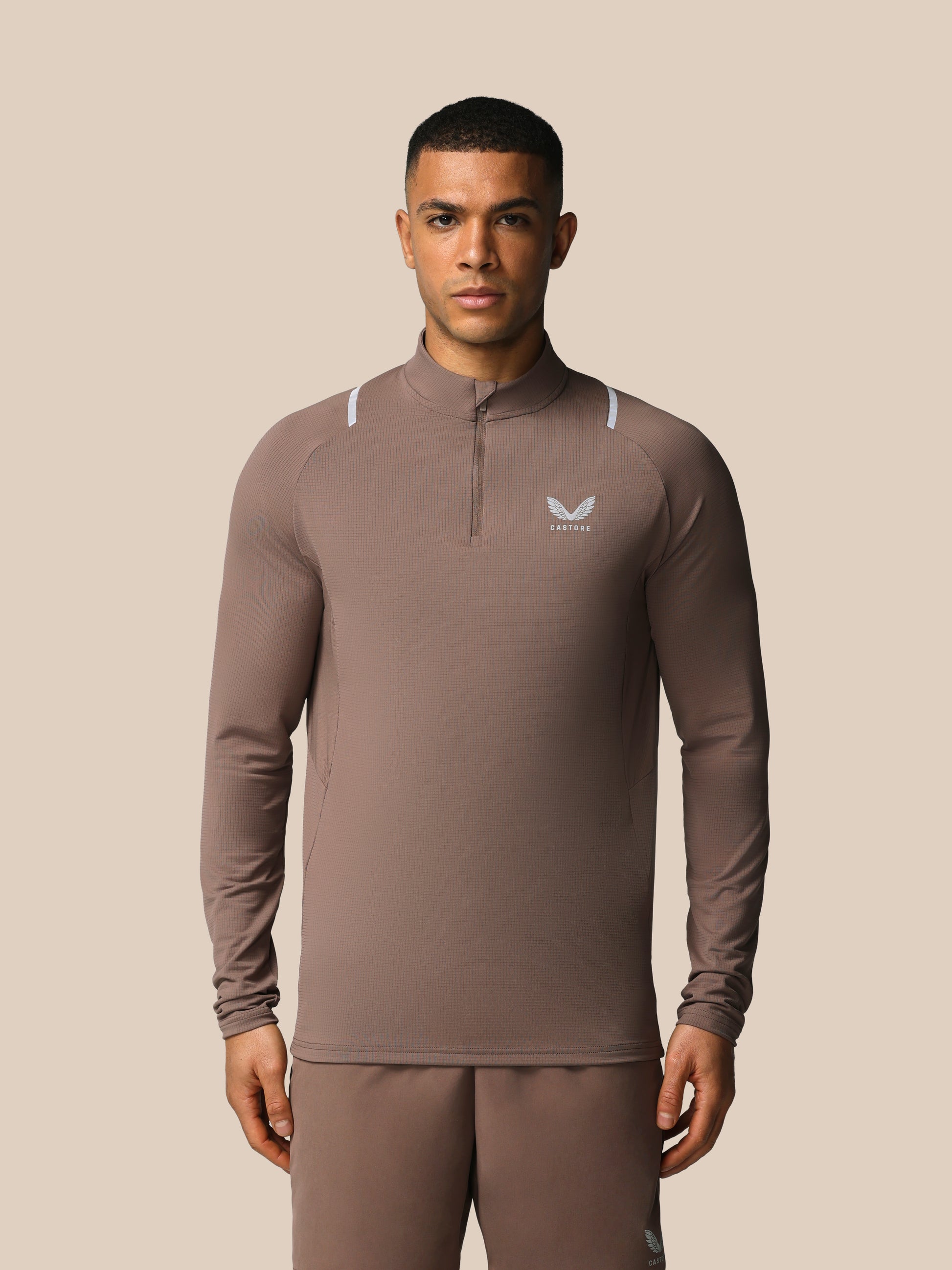Man wearing a brown athletic outfit with a logo on a beige background