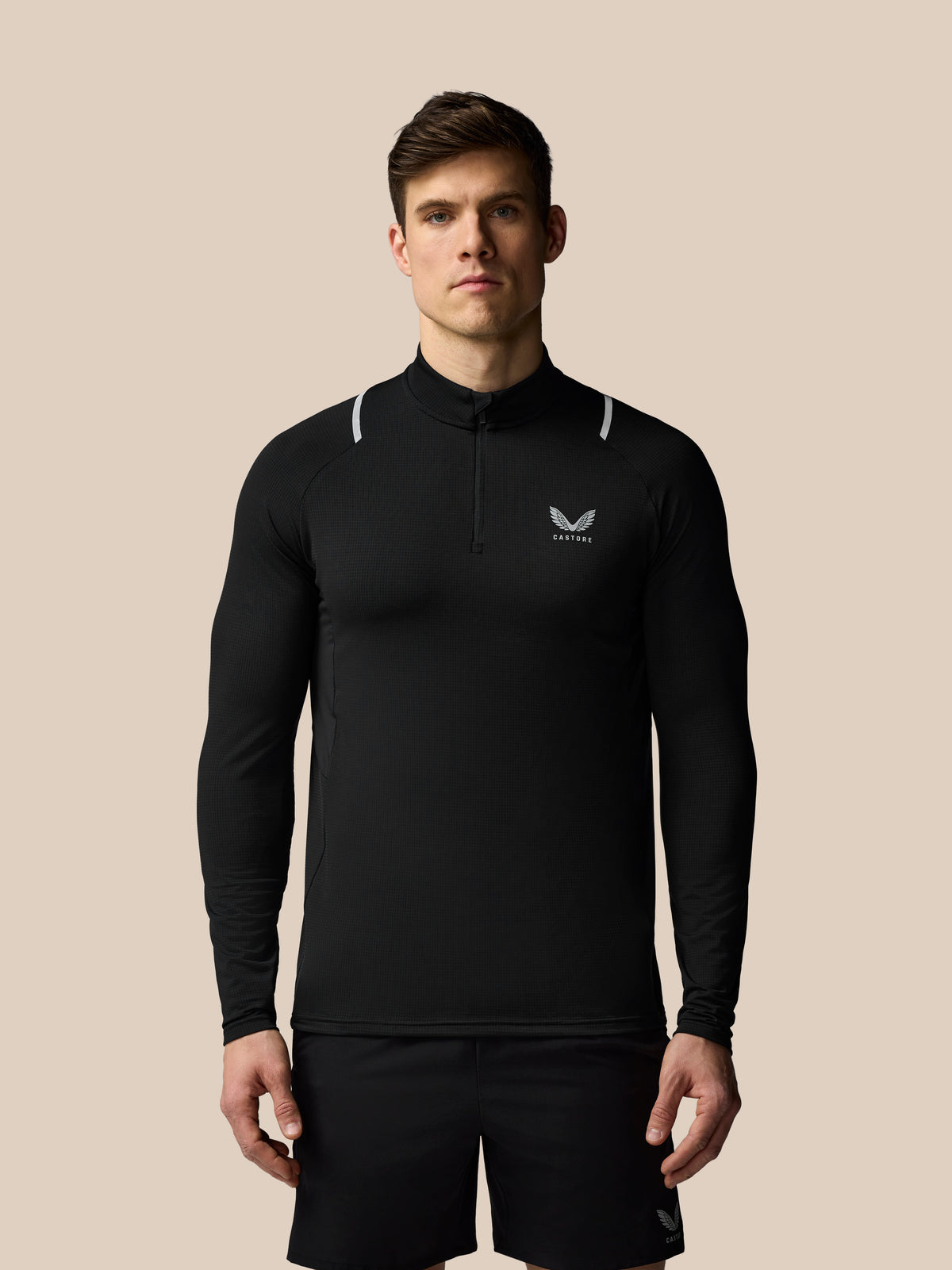 Man wearing a black long-sleeve athletic shirt with a logo on a beige background