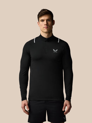 Man wearing a black long-sleeve athletic shirt with a logo on a beige background
