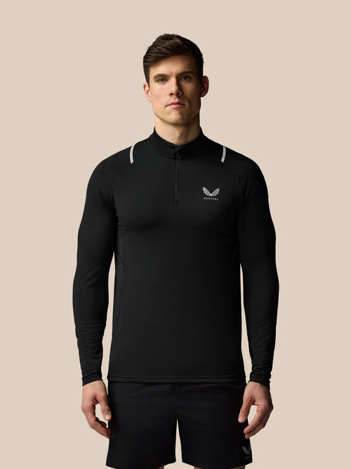 Man wearing a black long-sleeve athletic shirt with a logo on a beige background