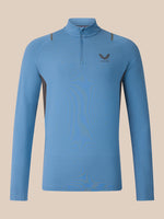 A light blue long-sleeve quarter-zip athletic top with a small dark gray wing logo and the brand name 'CASTORE' on the left chest, displayed against a solid beige background.
