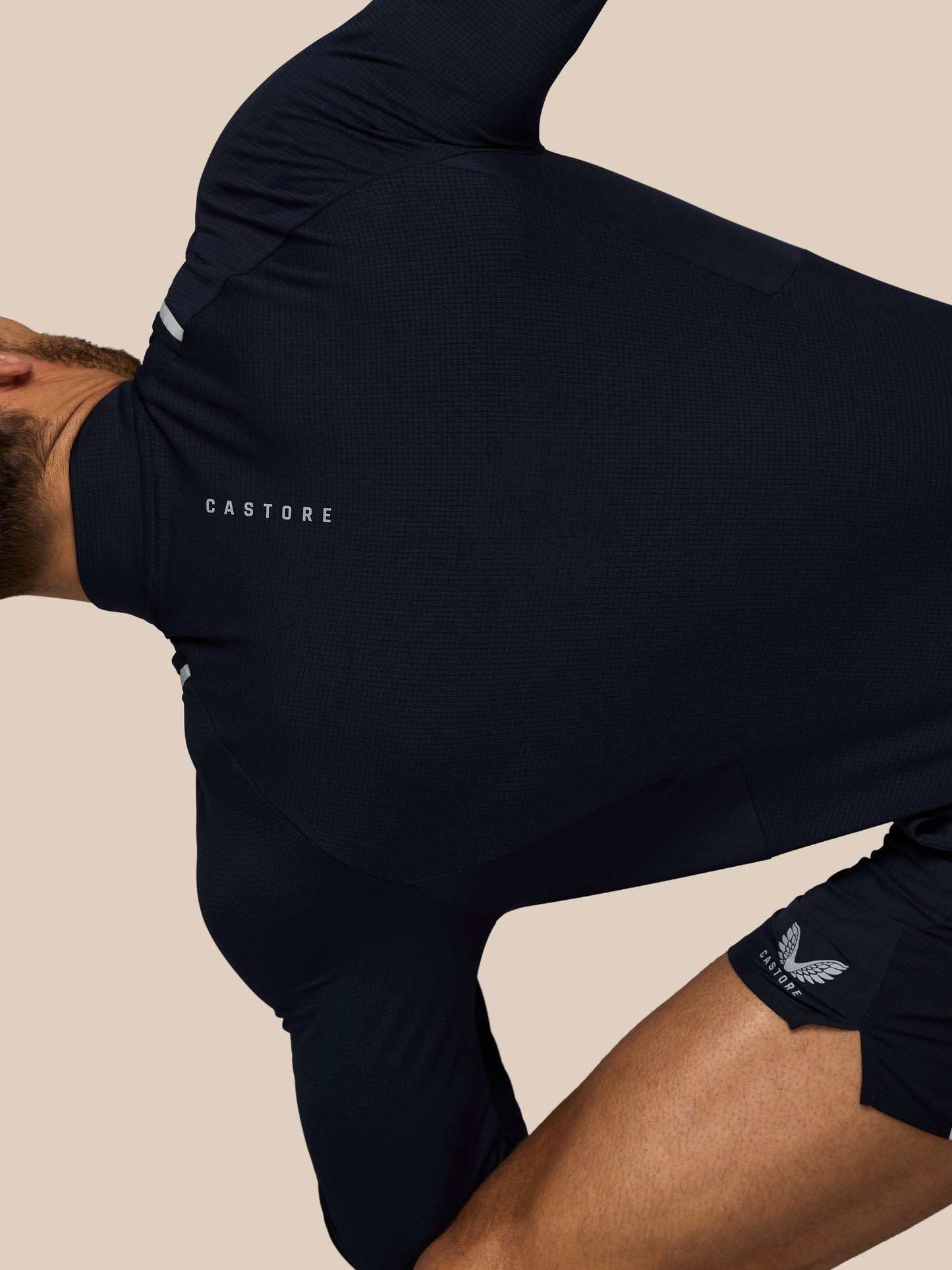 Person wearing a navy blue athletic outfit with 'Castore' branding on a beige background