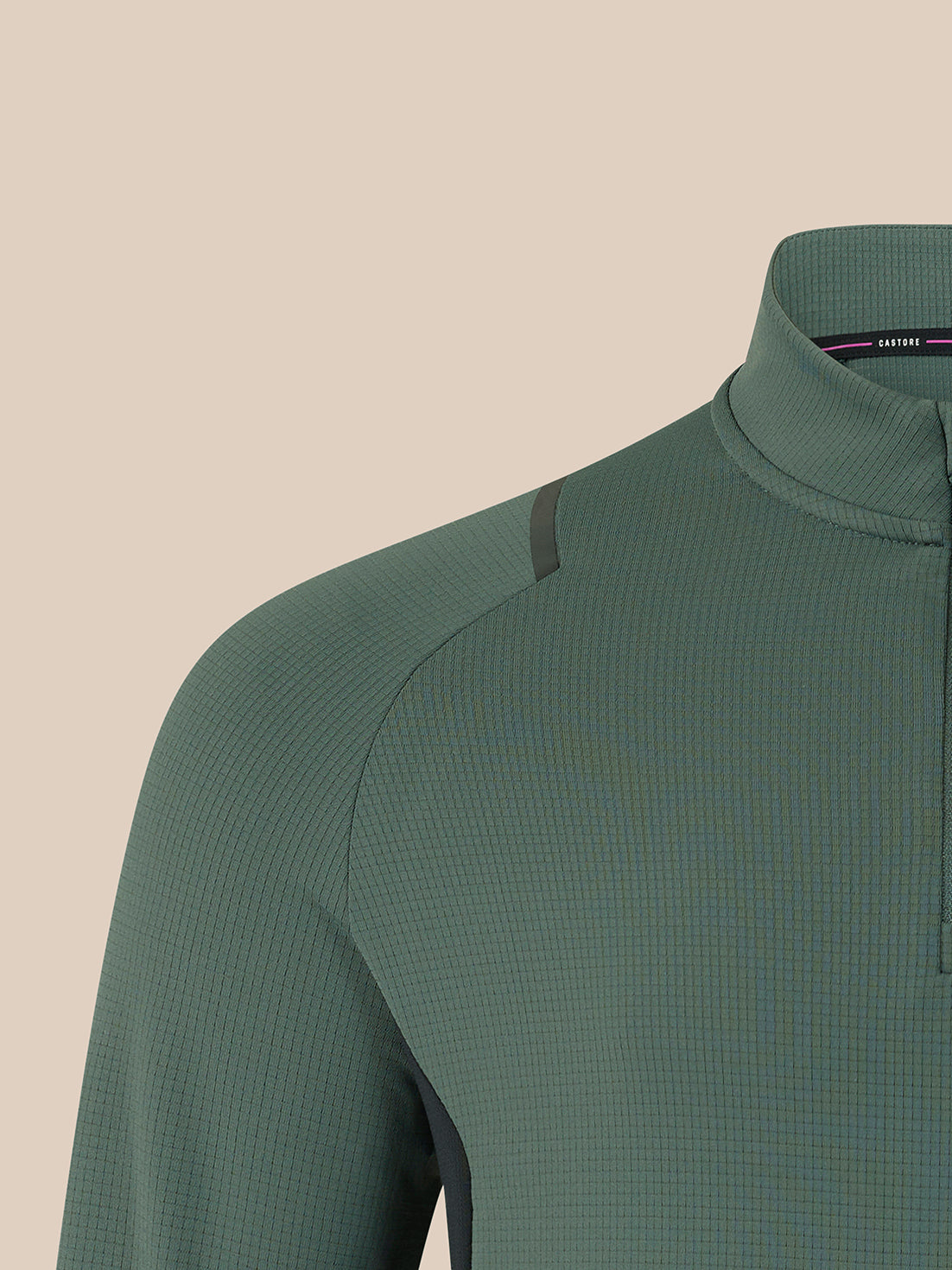Close-up of a long-sleeve quarter-zip athletic top in muted sage green, showing the collar, textured fabric, and shoulder seam against a plain beige background.