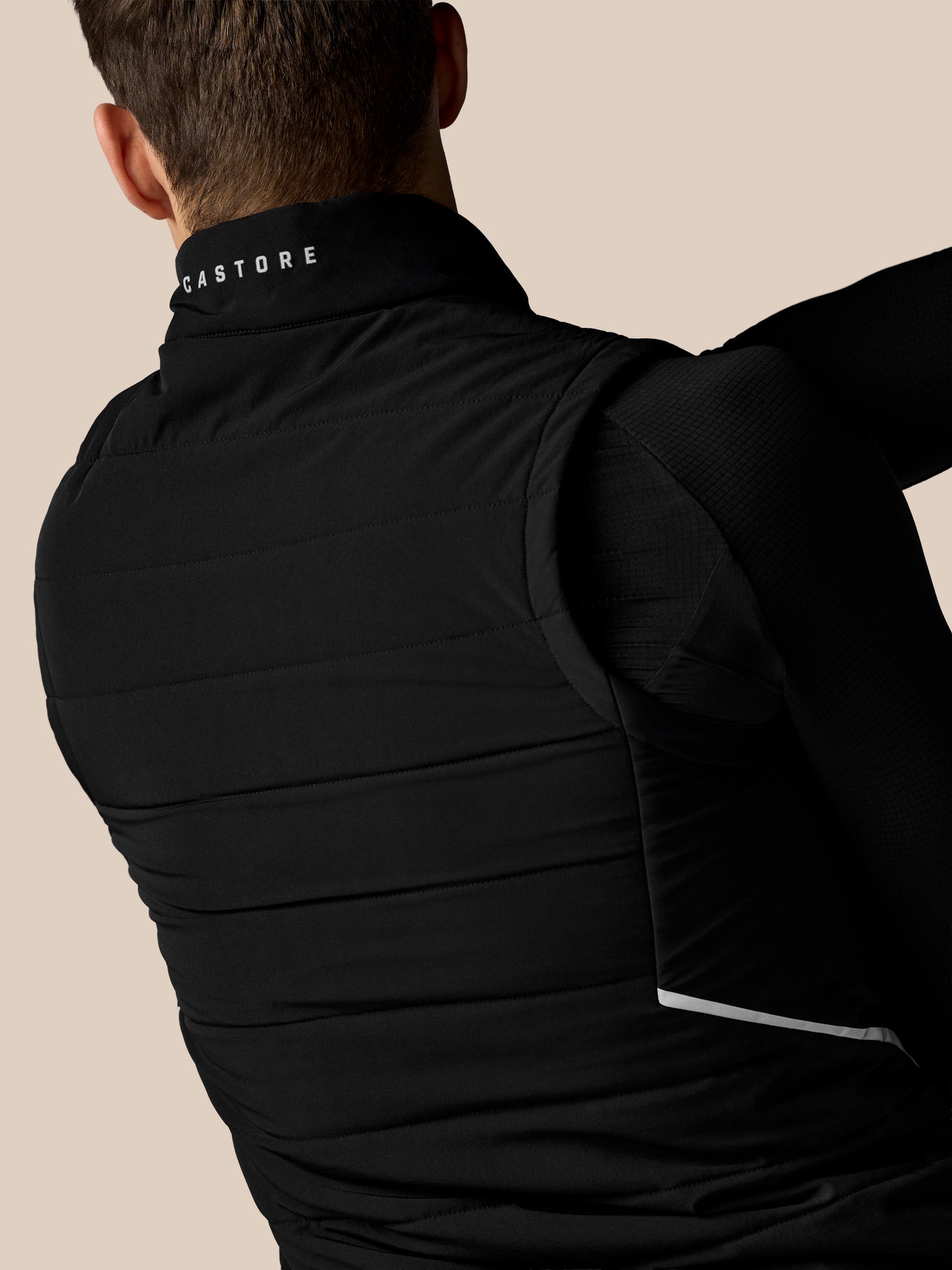 Person wearing a black puffer jacket with 'Castore' branding on a beige background