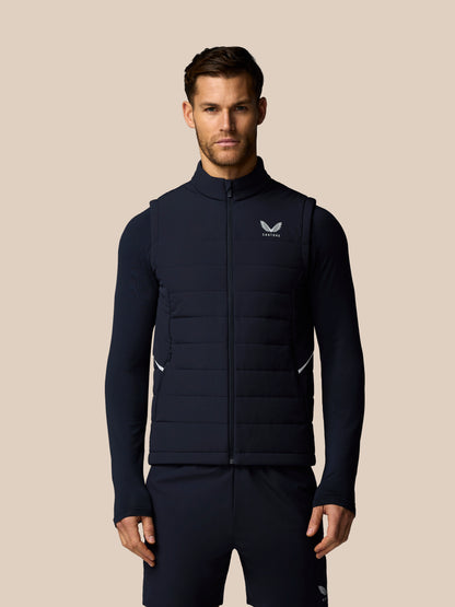 Man wearing a navy blue puffer vest with a brand logo on a beige background