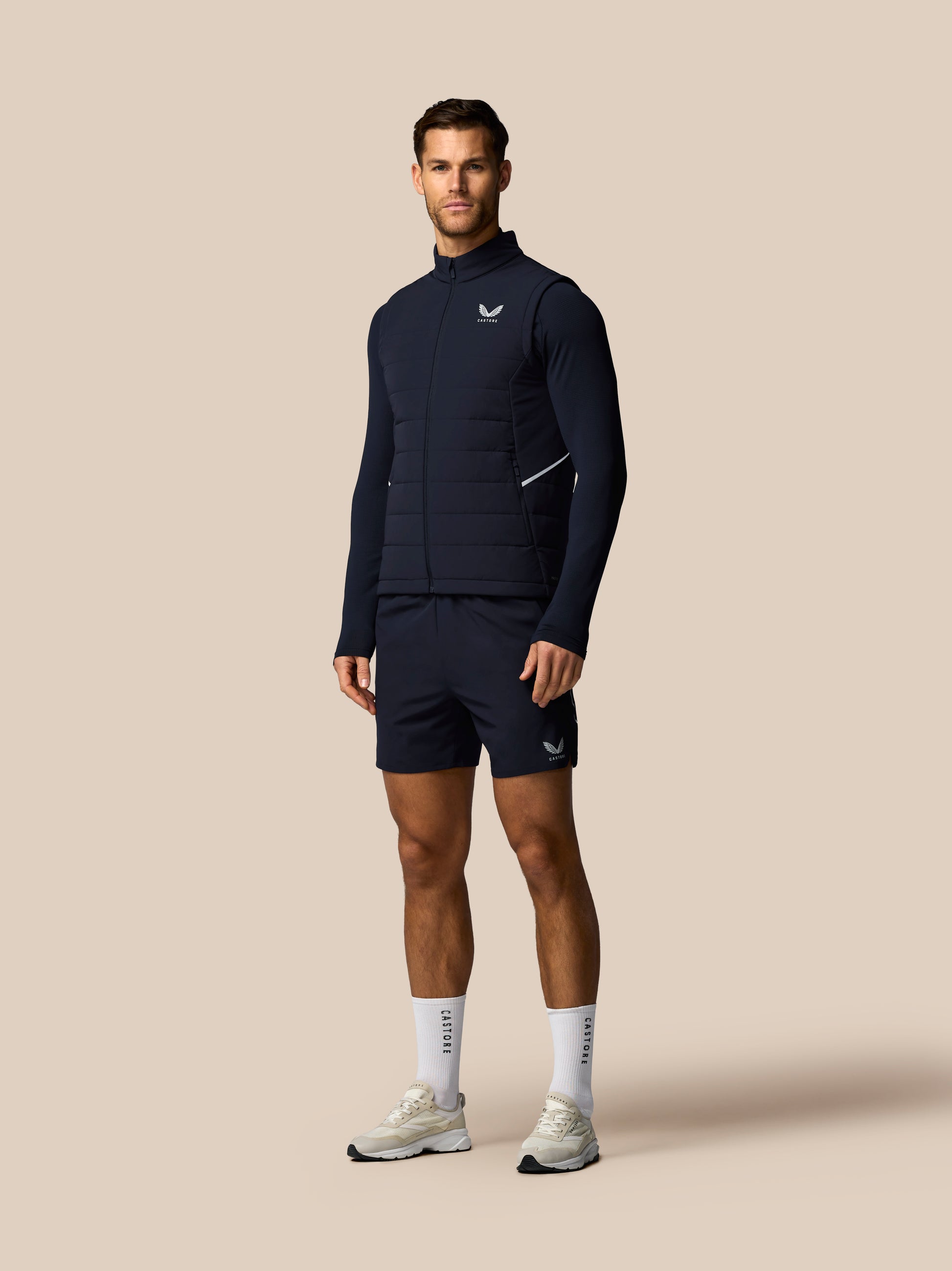 Man wearing a navy athletic outfit with a logo on a beige background
