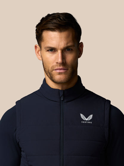 Man wearing a navy blue vest with a brand logo on a beige background