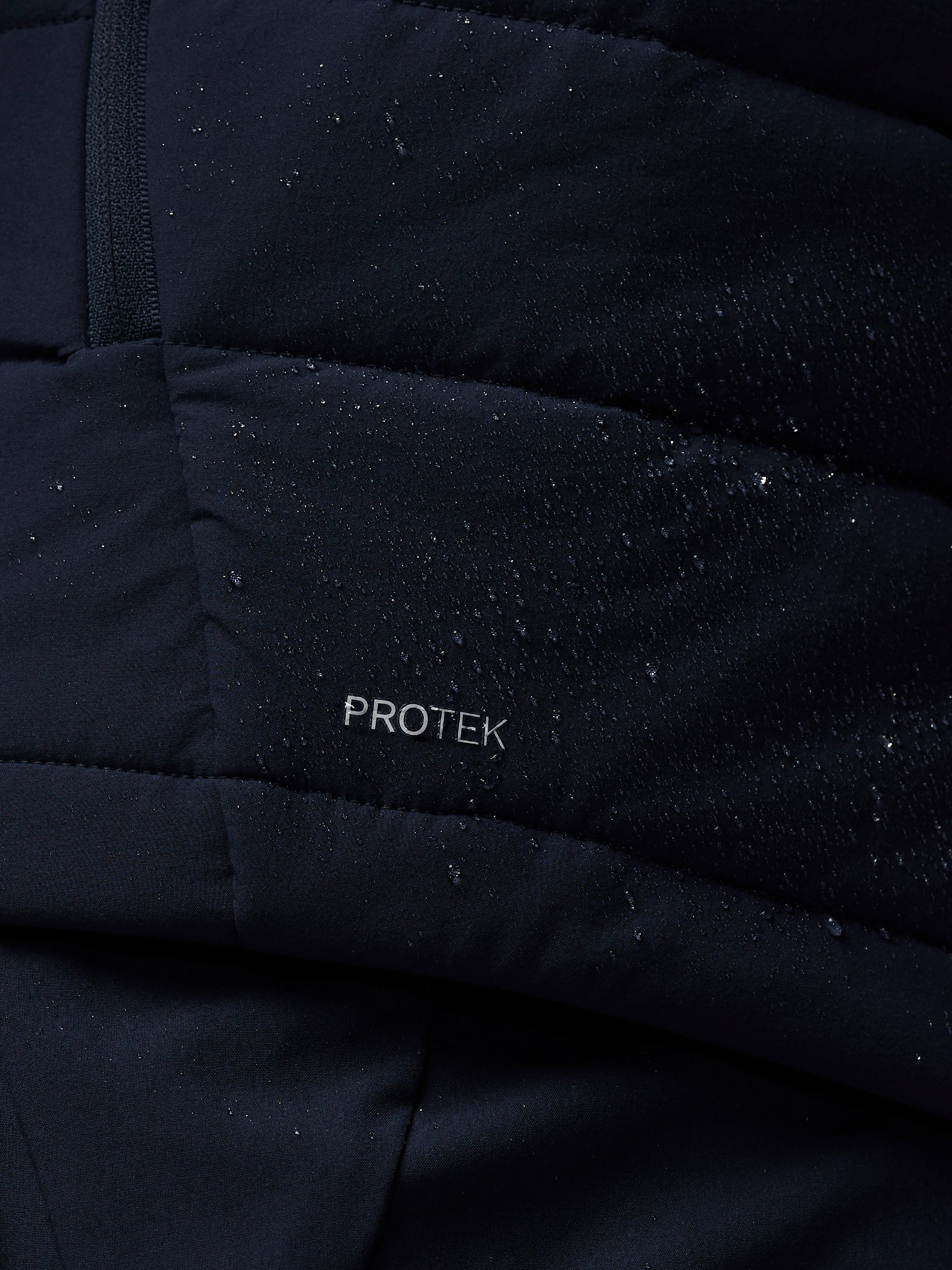 Close-up of a black quilted jacket with 'PROTEK' branding.
