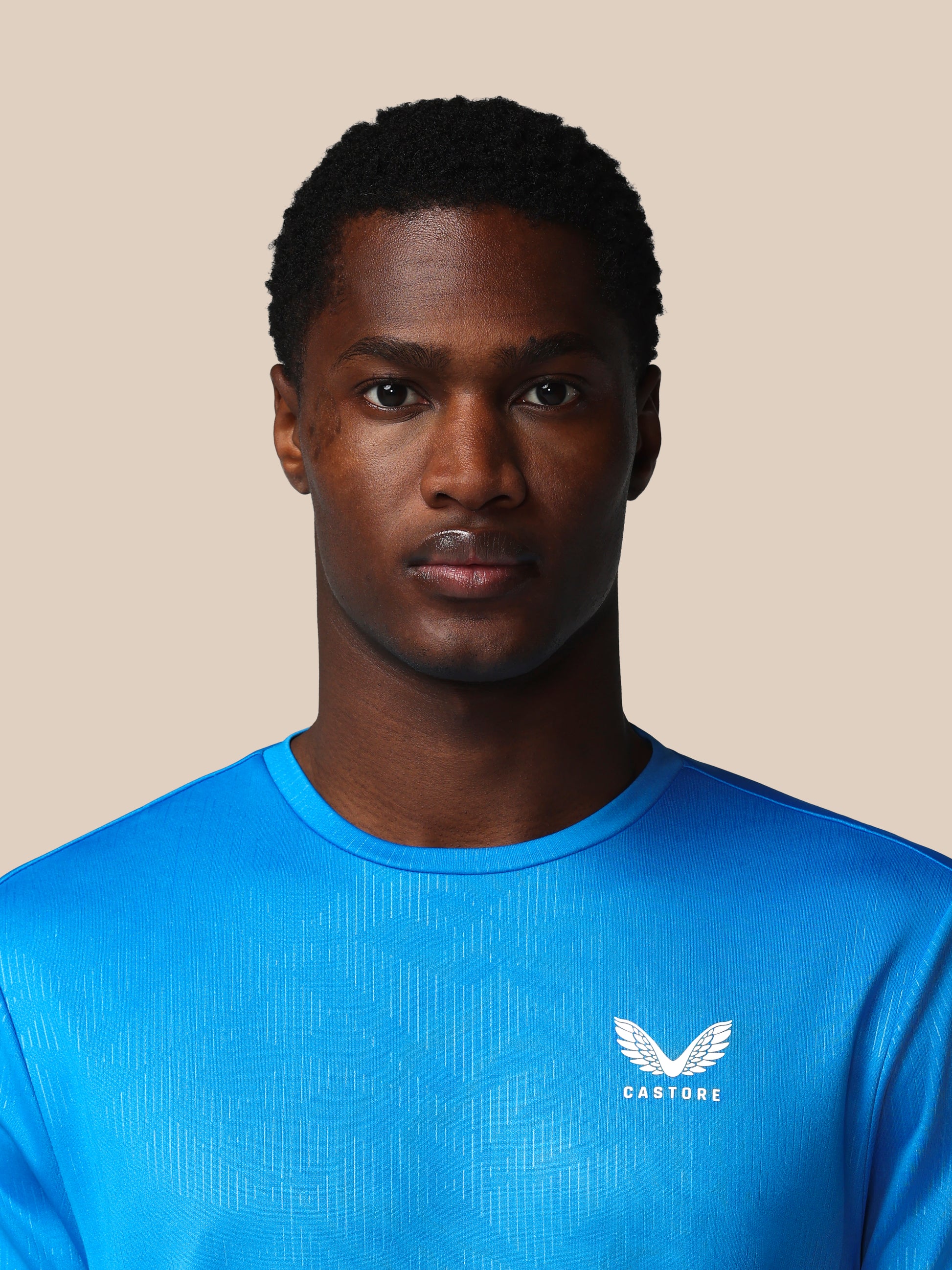 Man wearing a blue athletic shirt with a logo on a beige background