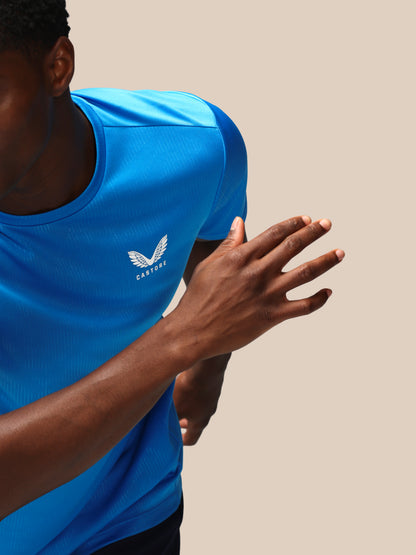 Person wearing a blue athletic shirt with a logo on a beige background