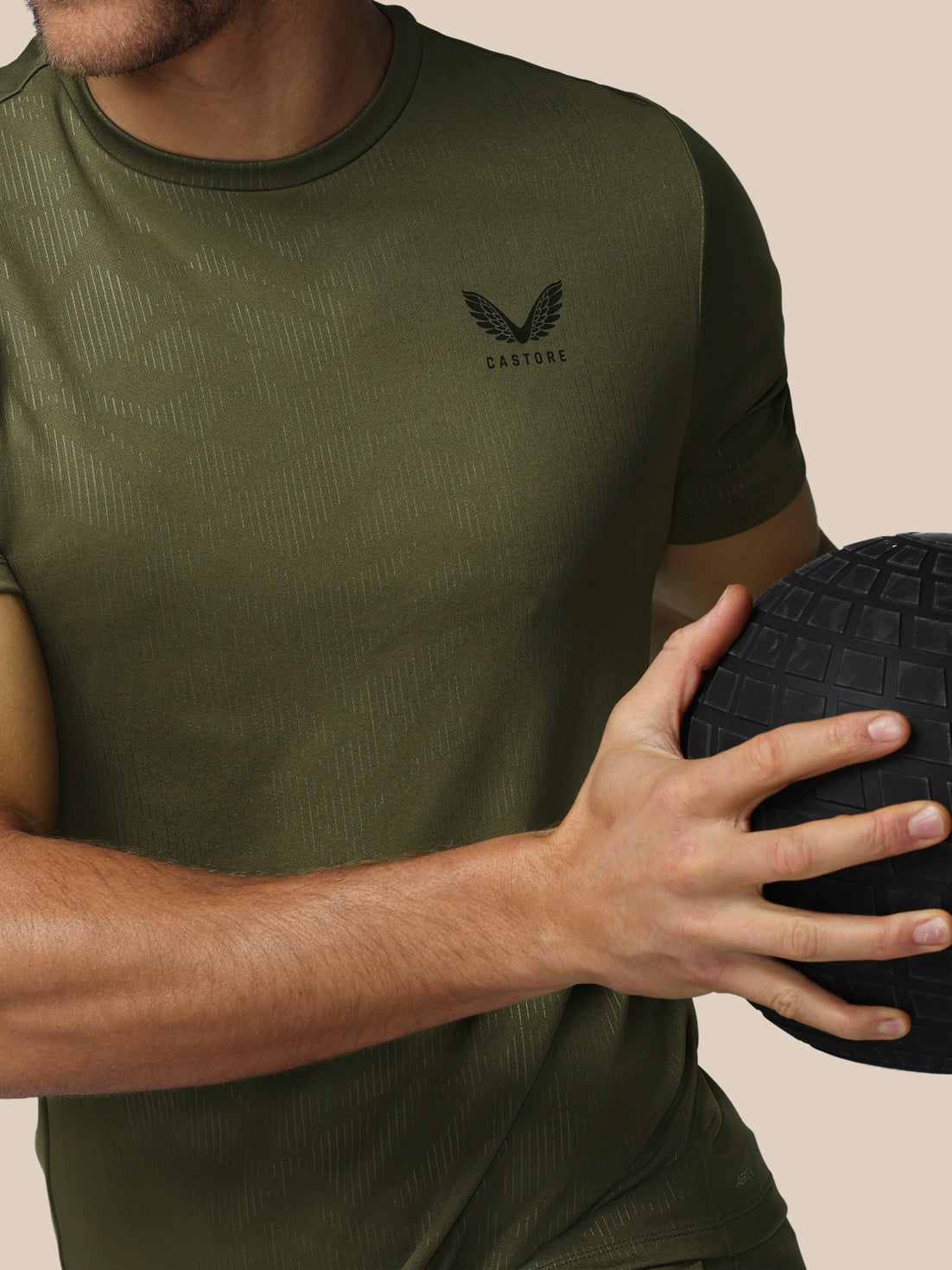 Person wearing a green t-shirt with a logo, holding a black ball against a beige background