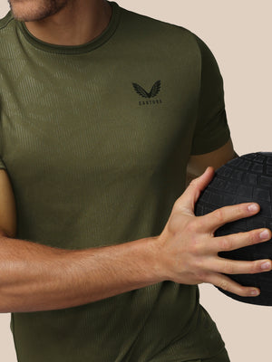 Person wearing a green t-shirt with a logo, holding a black ball against a beige background