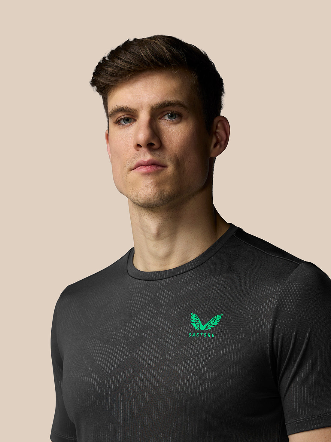 Man wearing a black athletic shirt with a green logo on a beige background
