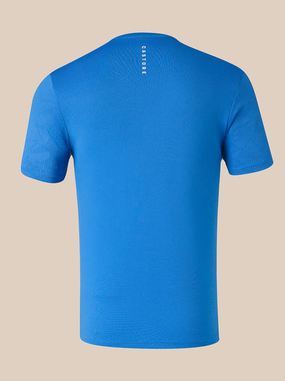 A blue short-sleeve athletic t-shirt shown from the back, featuring a vertical white 'CASTORE' logo printed on the upper back, set against a solid beige background.