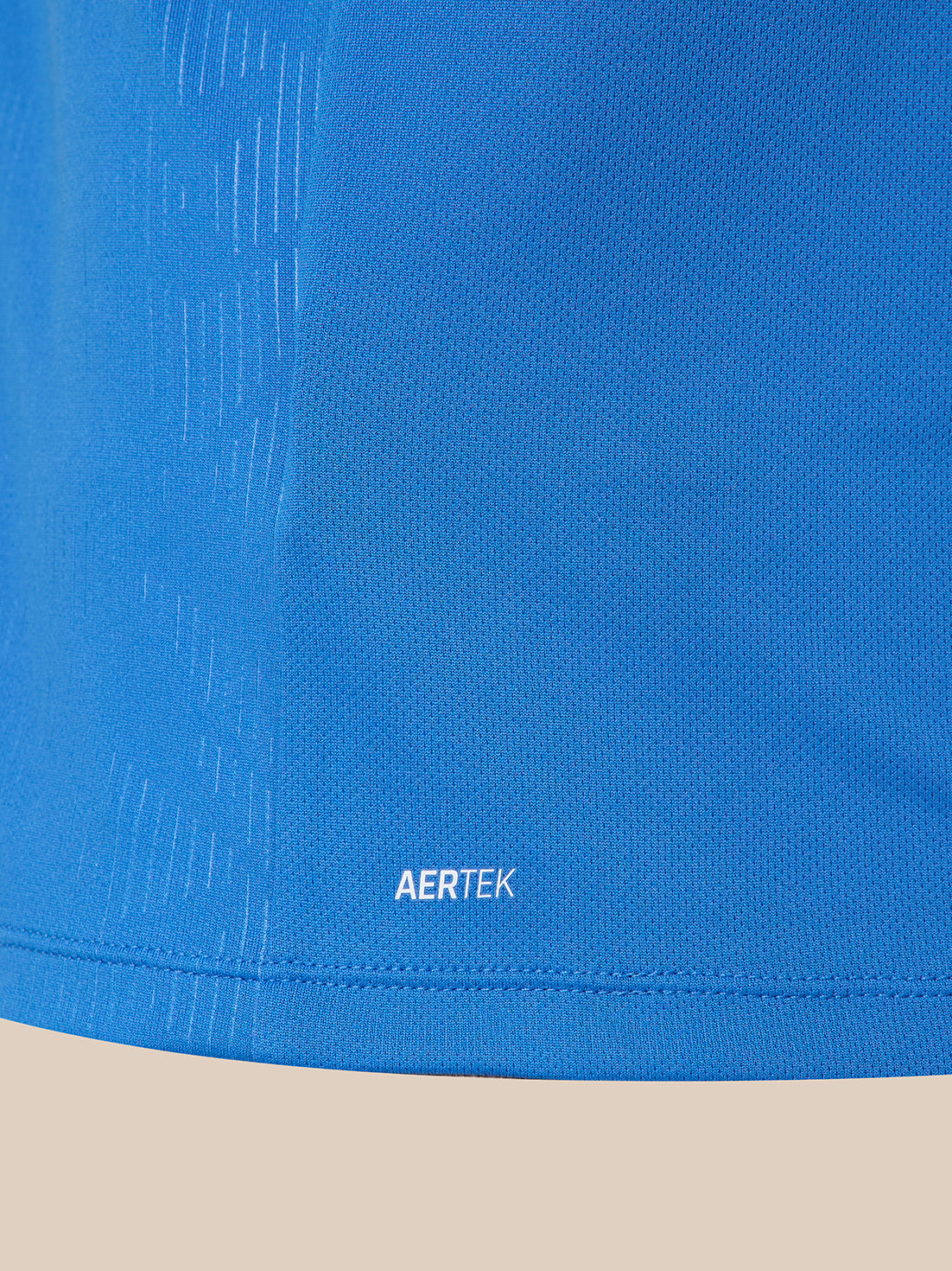Close-up of a blue athletic fabric with a subtle textured pattern and a small white AERTEK logo near the hem, shown against a light beige background.