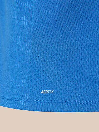 Close-up of a blue athletic fabric with a subtle textured pattern and a small white AERTEK logo near the hem, shown against a light beige background.