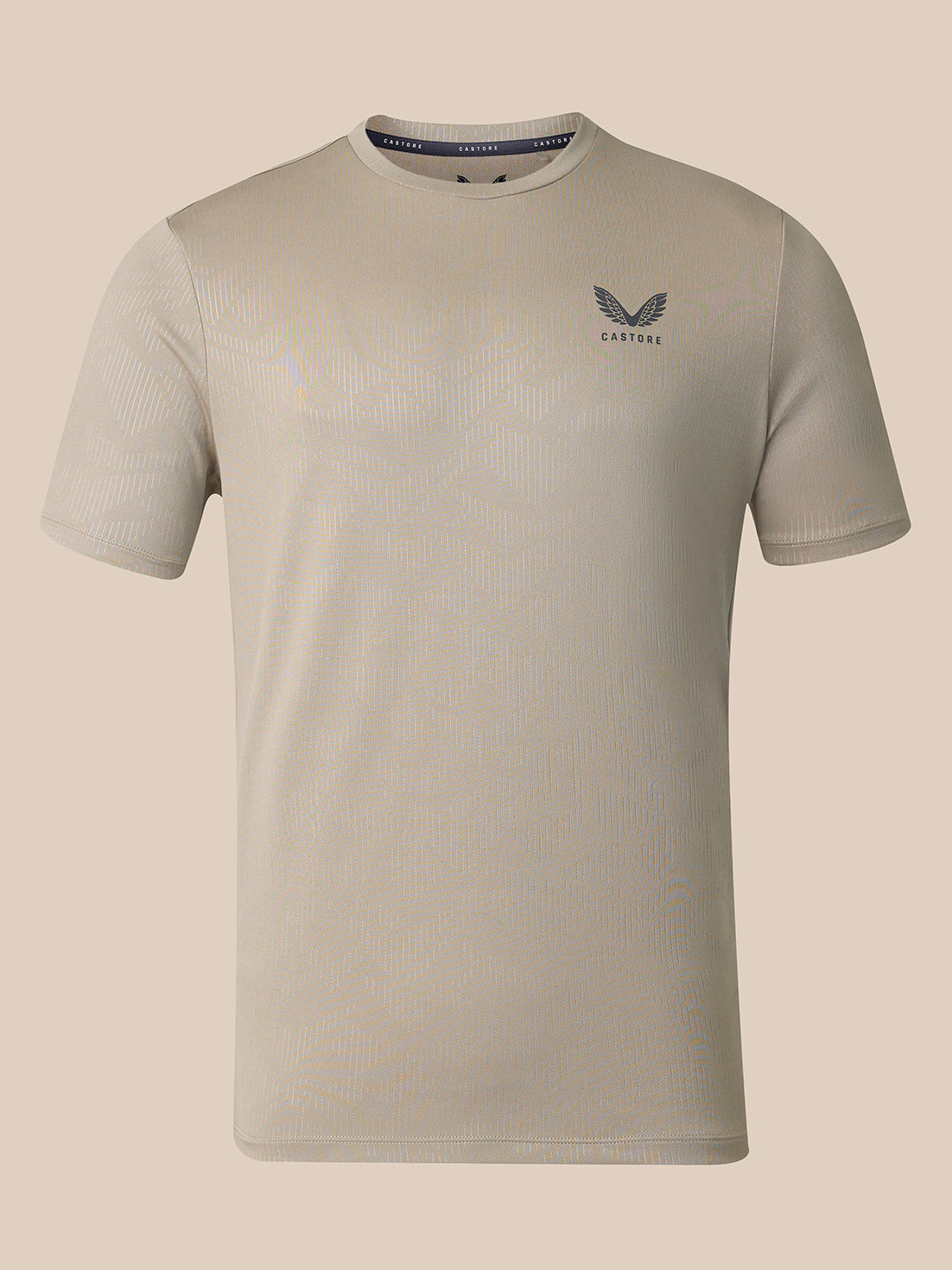 A light beige short-sleeve athletic t-shirt with a subtle ribbed texture, featuring a dark gray wing logo and the brand name 'CASTORE' On the left chest, displayed against a solid beige background.