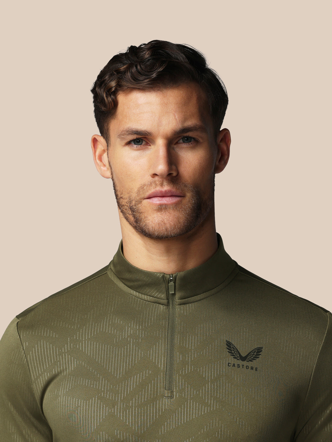 Man wearing a green athletic jacket with a brand logo on a beige background