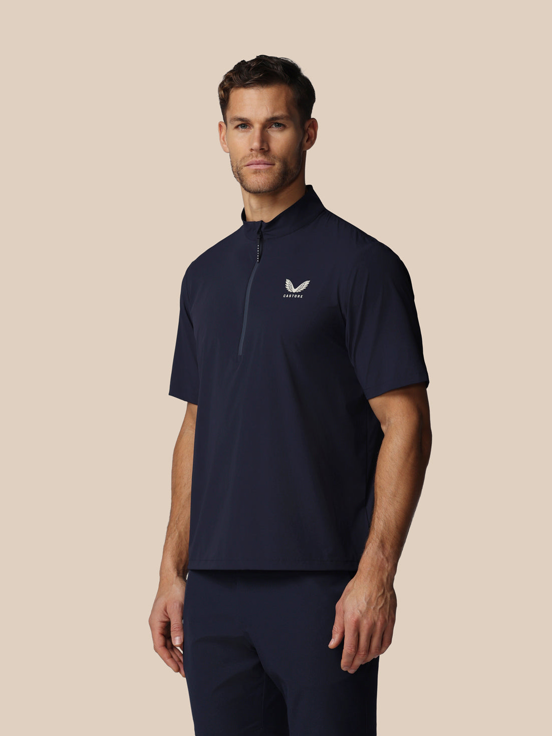 Man wearing a navy blue polo shirt with a logo on a beige background