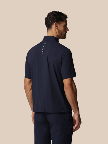 Man wearing a navy blue polo shirt with a Castore wordmark on the back against a beige background