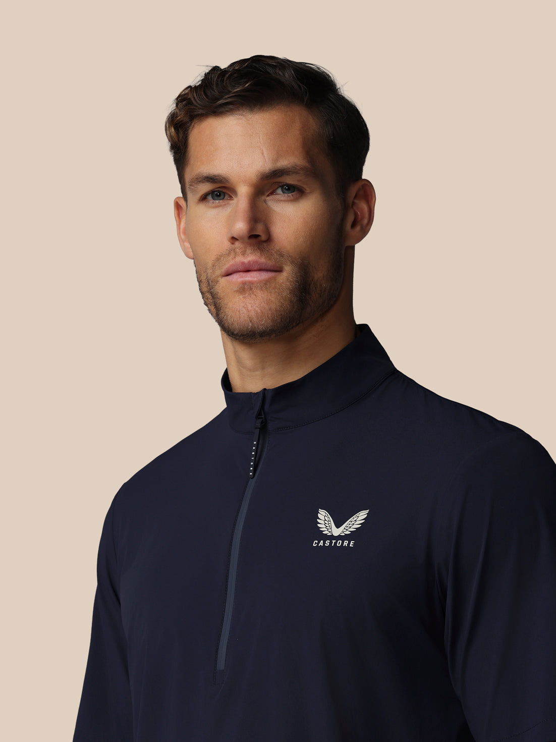 Man wearing a navy blue quarter-zip sweatshirt with Castore logo on a beige background