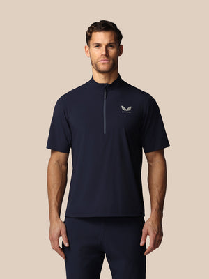 Man wearing a navy blue athletic shirt with Castore logo on a beige background