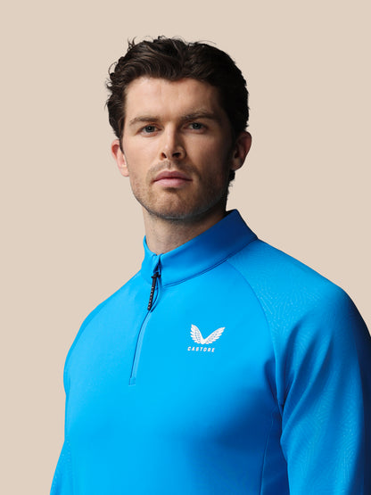 Man wearing a blue golf jacket with Castore logo on a beige background