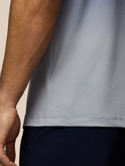 Close-up of a person wearing a gray patterned shirt with a visible brand logo.