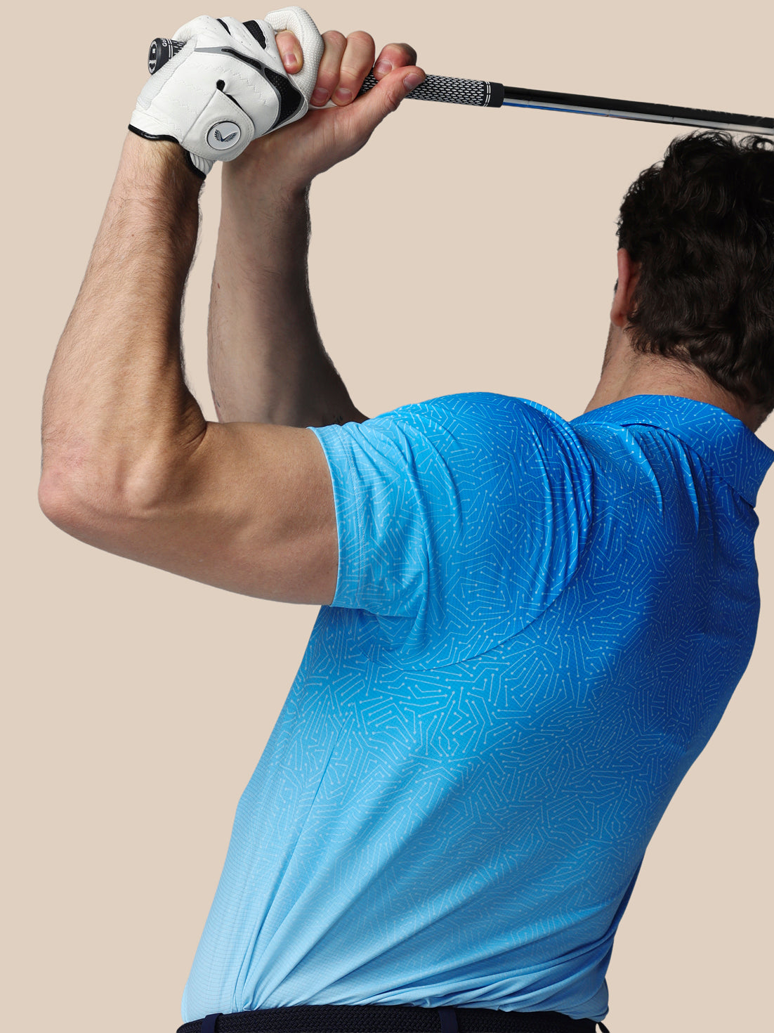 Person in a blue shirt holding a golf club against a beige background