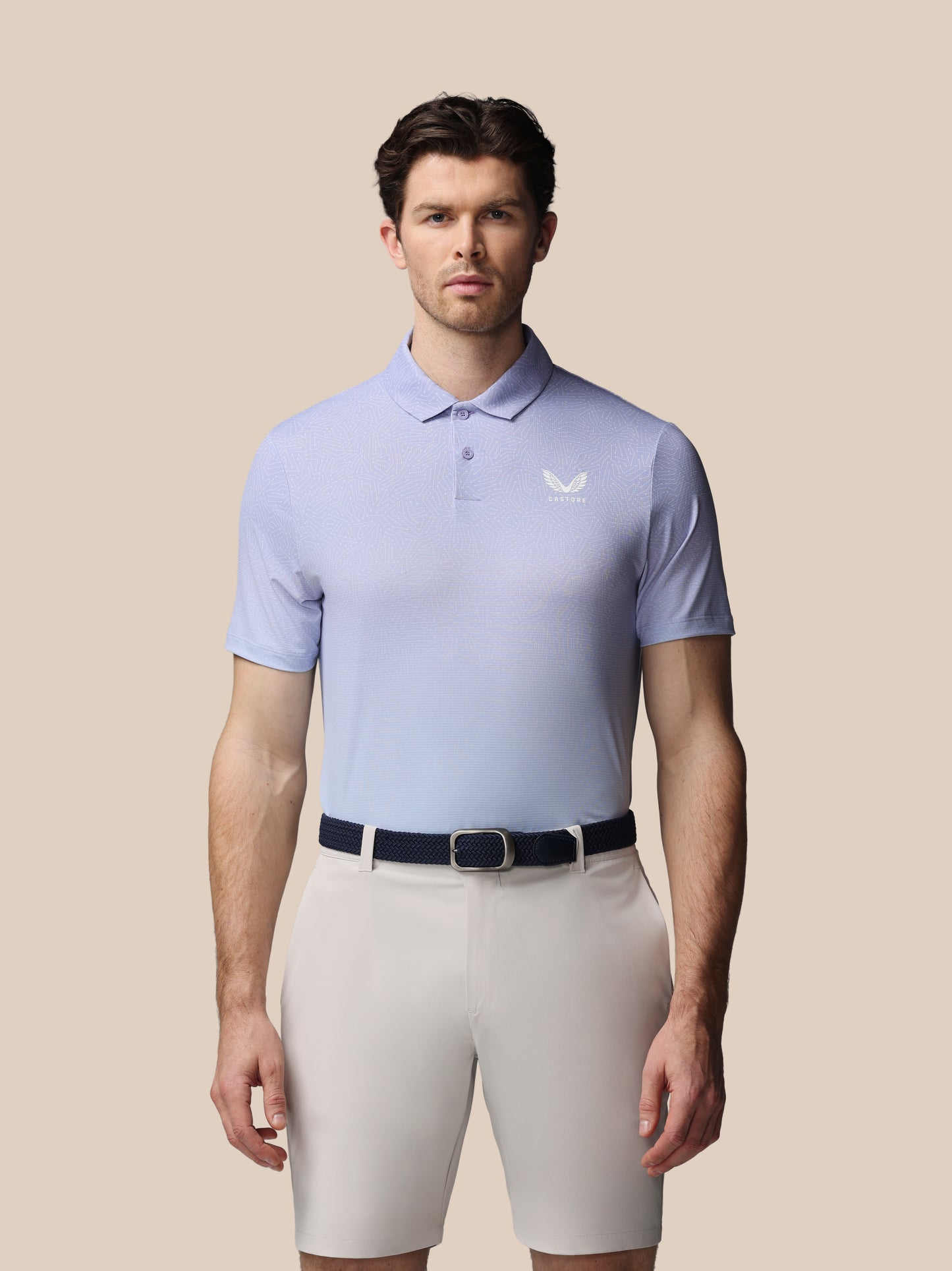 Man wearing a light purple polo shirt and beige shorts on a beige background