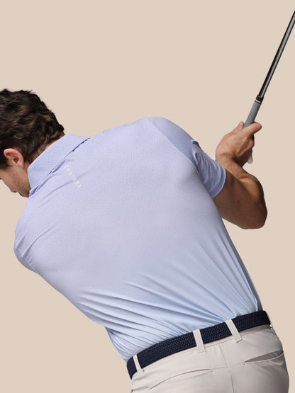 Man in light blue shirt and beige pants swinging a golf club against a beige background