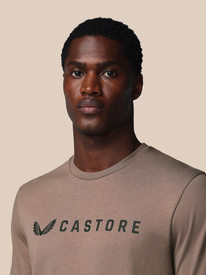 Man wearing a brown t-shirt with 'CASTORE' logo on a beige background