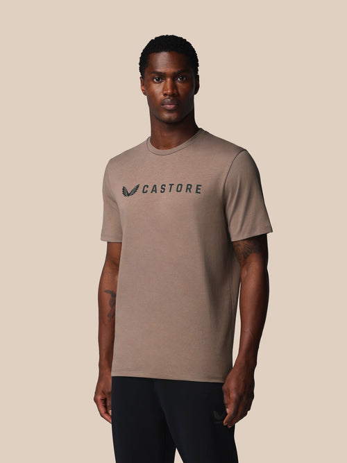 Man wearing a brown t-shirt with 'Castore' logo on a beige background