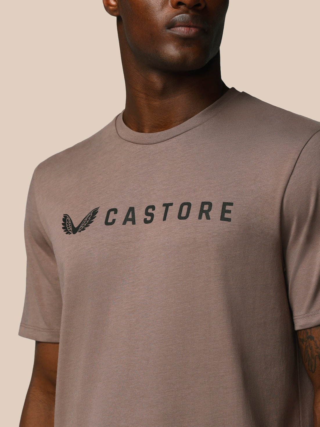 Man wearing a brown t-shirt with 'CASTORE' logo on a beige background