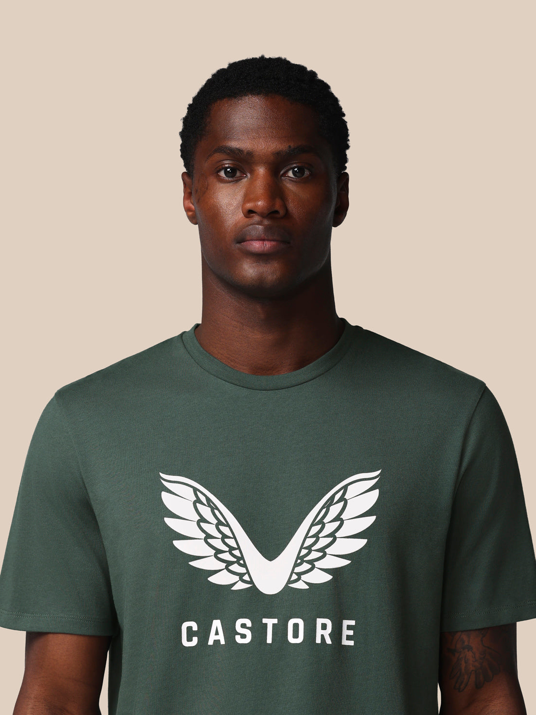 Man wearing a green t-shirt with a white logo and 'CASTORE' text on a beige background