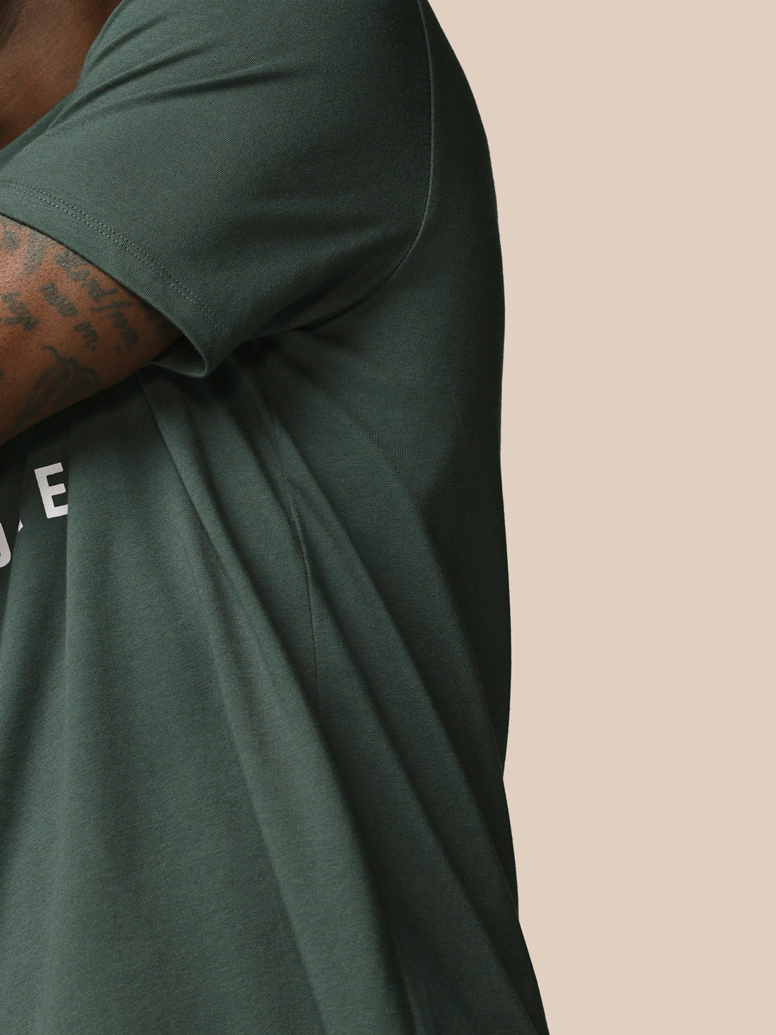Person wearing a dark green t-shirt with a visible brand logo on a beige background