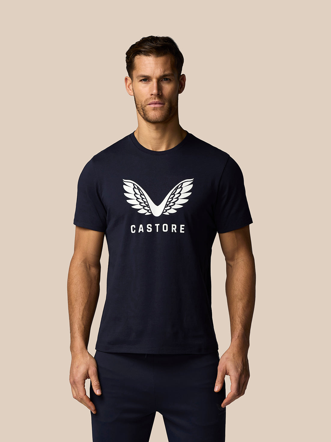 Man wearing a navy blue t-shirt with a logo and text on a beige background