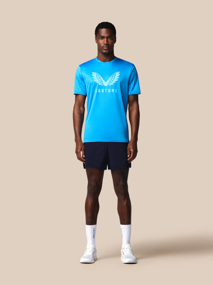 Man wearing a blue athletic shirt with a logo and dark shorts on a beige background