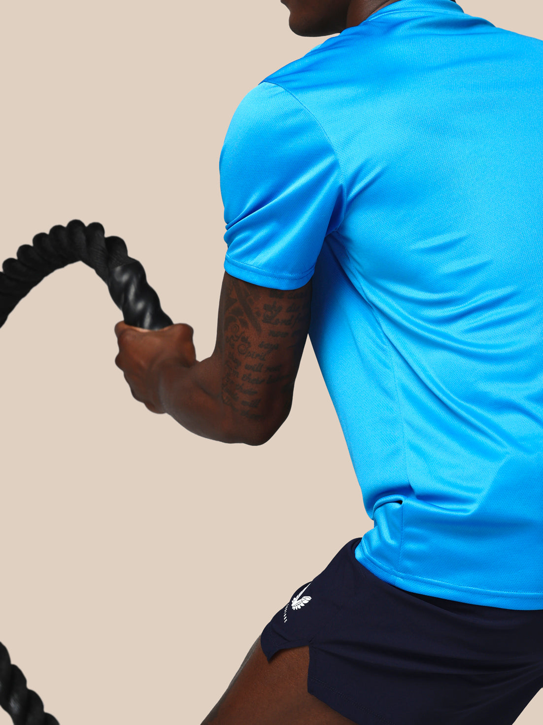 Person wearing a blue athletic shirt and black shorts, holding a resistance band against a beige background